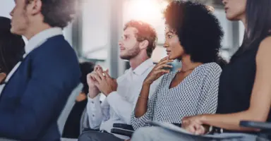 Grupo de profissionais assistindo e aplaudindo durante um evento corporativo, ilustrando as imersões em hubs e ecossistemas de inovação da MEI.